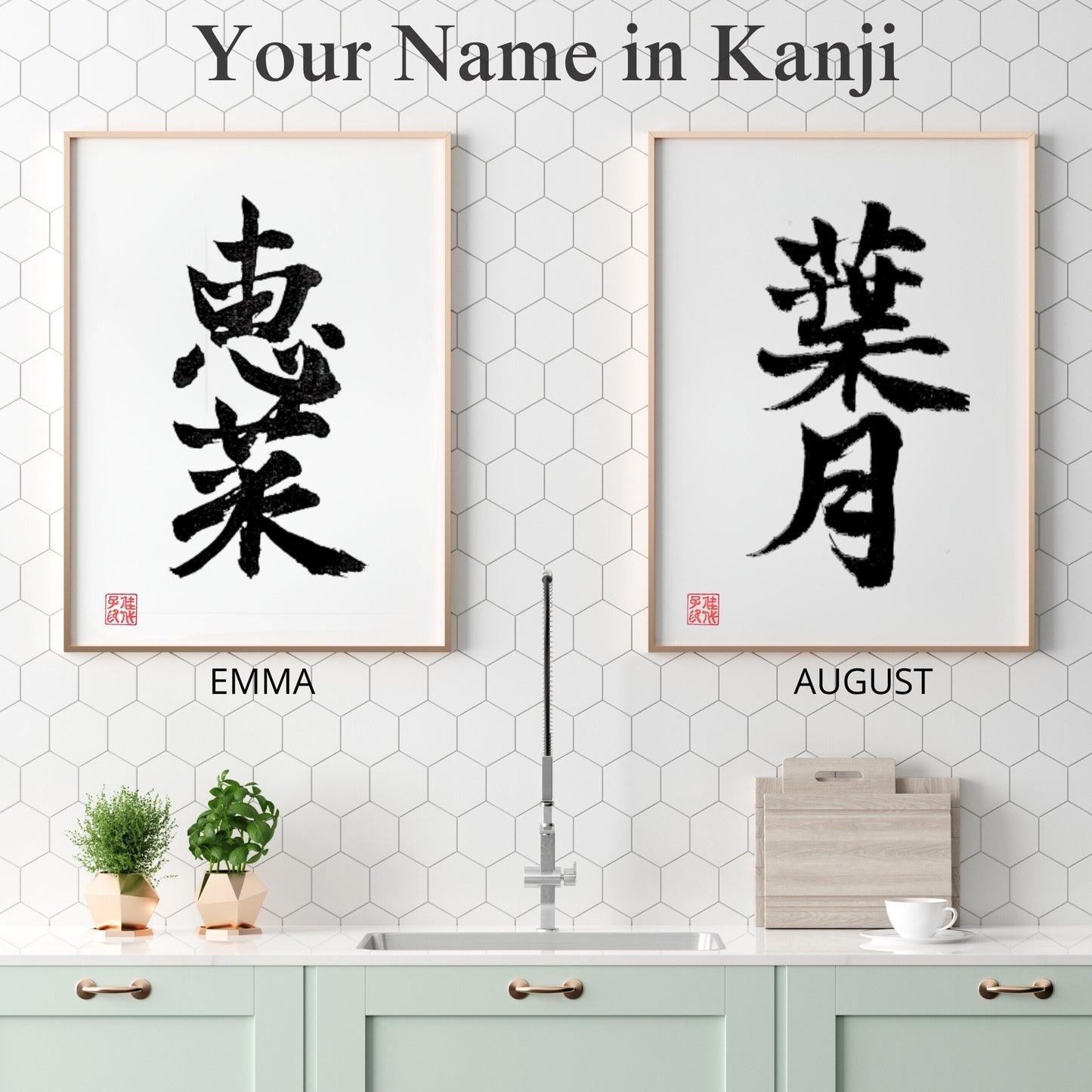 Two framed Kanji name art pieces for "EMMA" and "AUGUST" displayed side-by-side in a clean, white modern kitchen with honey-comb tile back-splash.