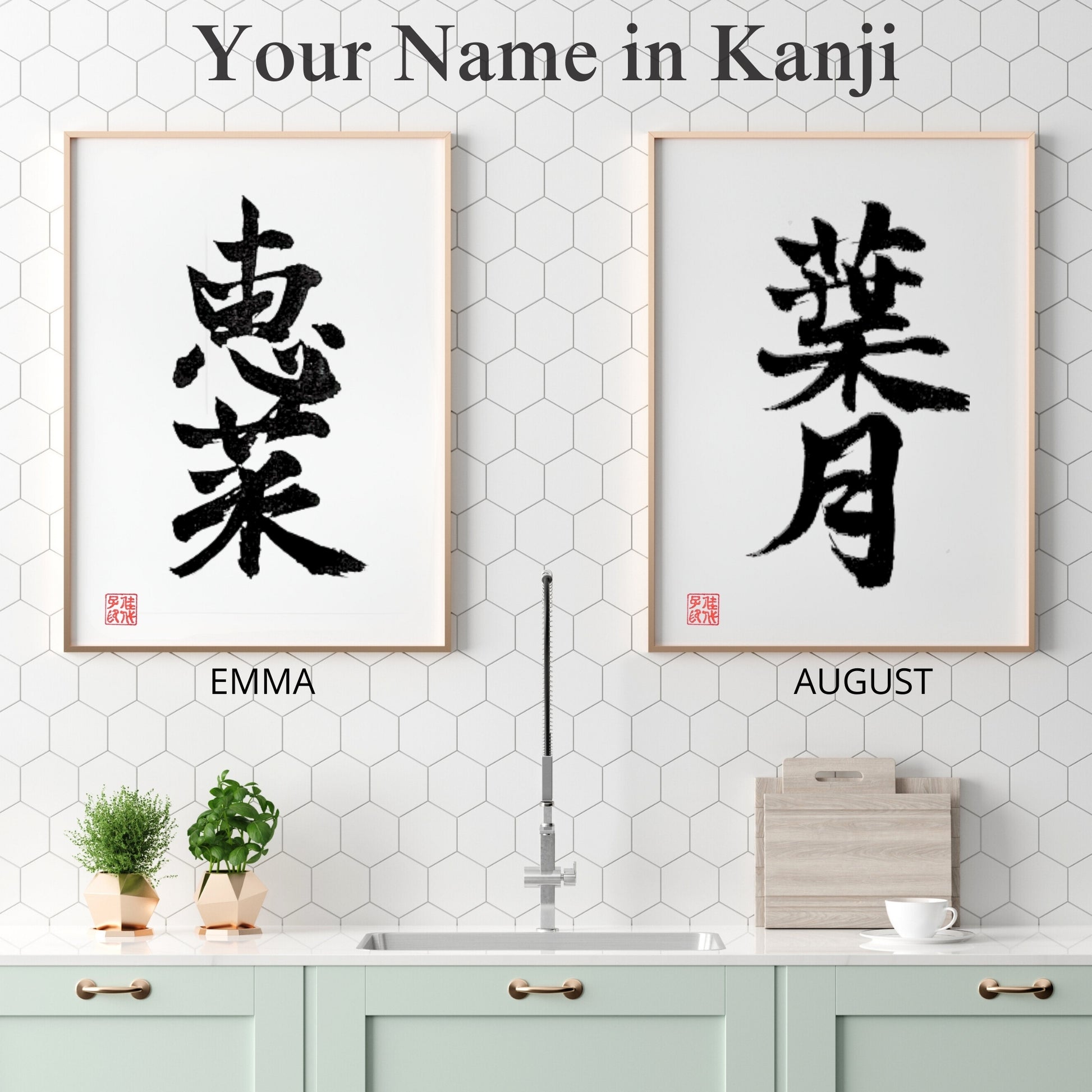 Two framed Kanji name art pieces for "EMMA" and "AUGUST" displayed side-by-side in a clean, white modern kitchen with honey-comb tile back-splash.