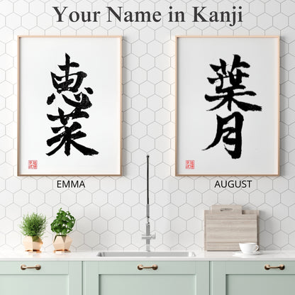 Two framed Kanji name art pieces for "EMMA" and "AUGUST" displayed side-by-side in a clean, white modern kitchen with honey-comb tile back-splash.