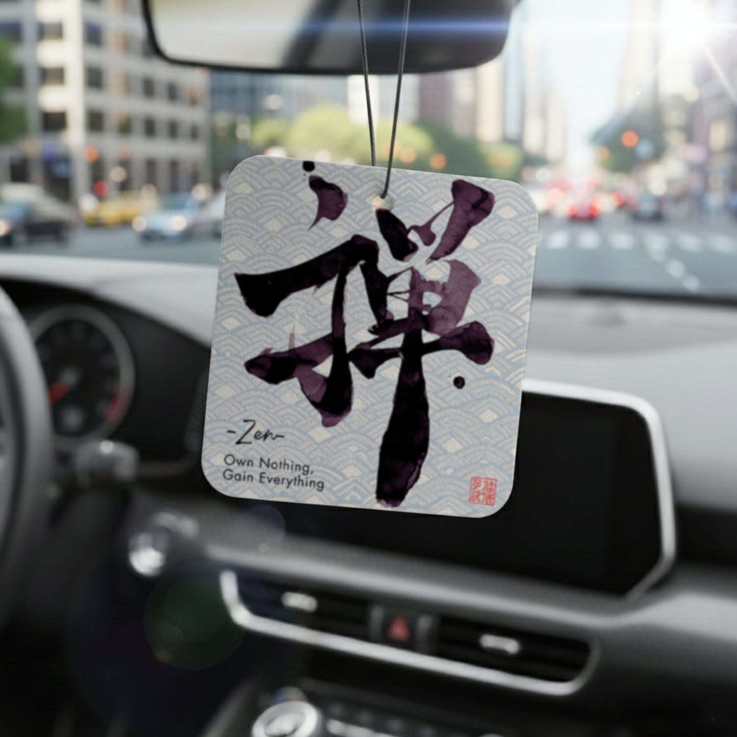 Car air freshener with Zen symbol hanging from a car's rearview mirror.