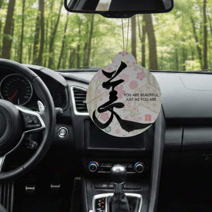 Car air freshener with motivational quote hanging from a car's rearview mirror in a forest setting