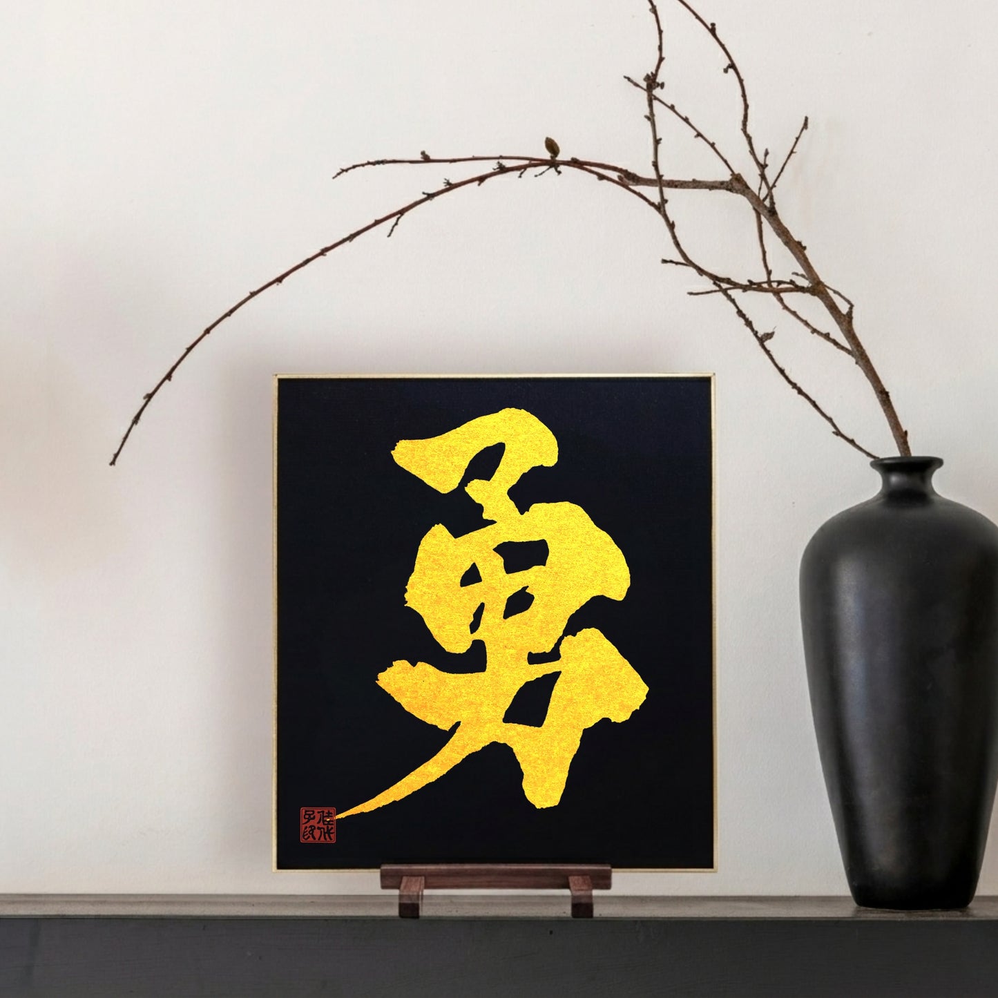 Gold Japanese calligraphy on a black background with a black vase and branch on a white wall
