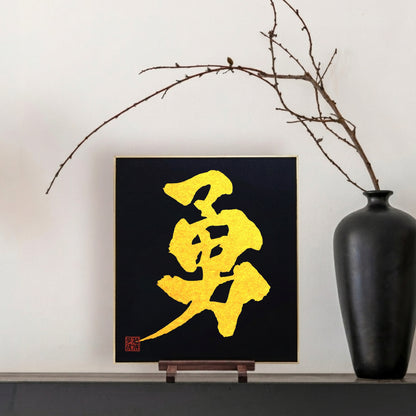 Gold Japanese calligraphy on a black background with a black vase and branch on a white wall