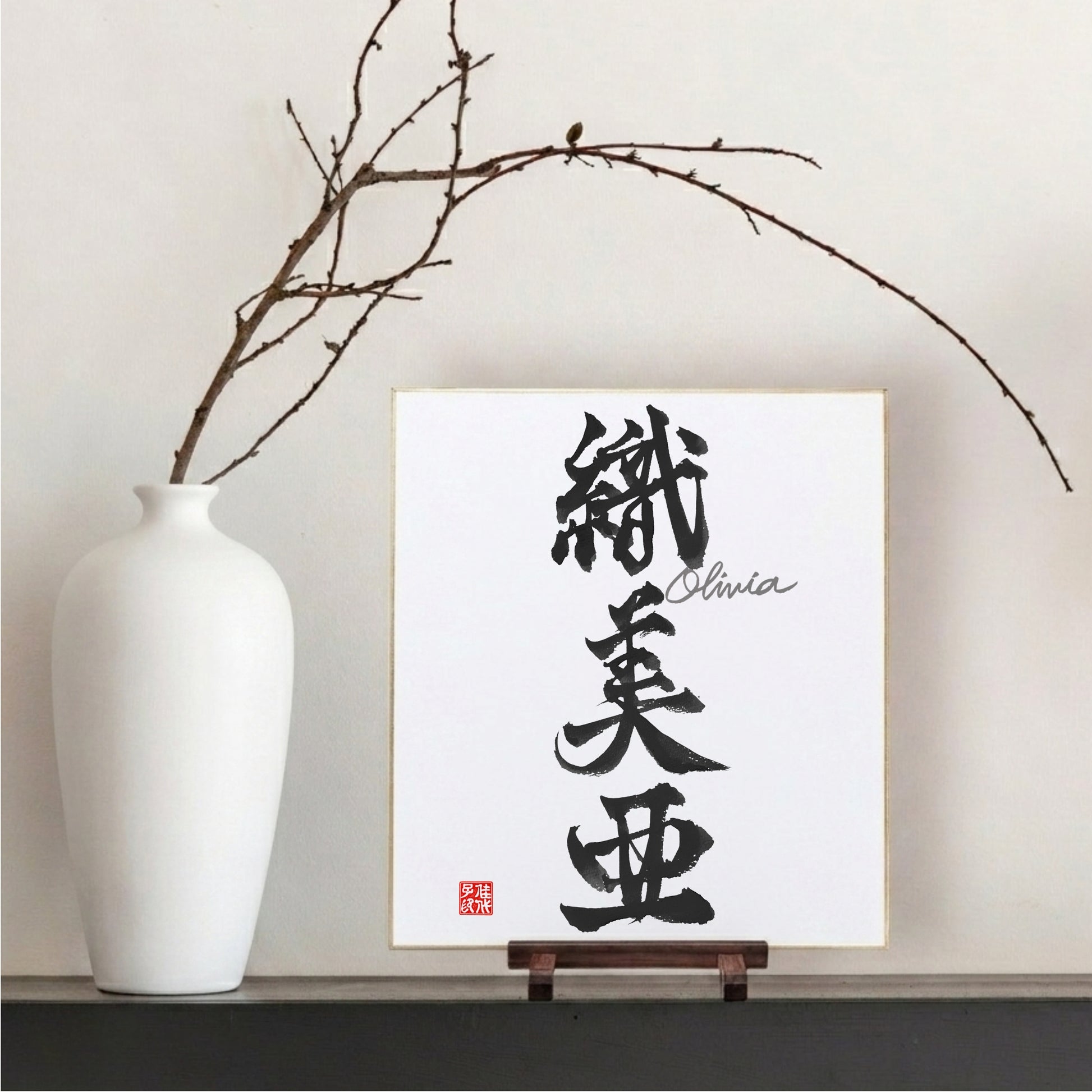 Japanese calligraphy artwork on a stand with a white vase and branches in the background